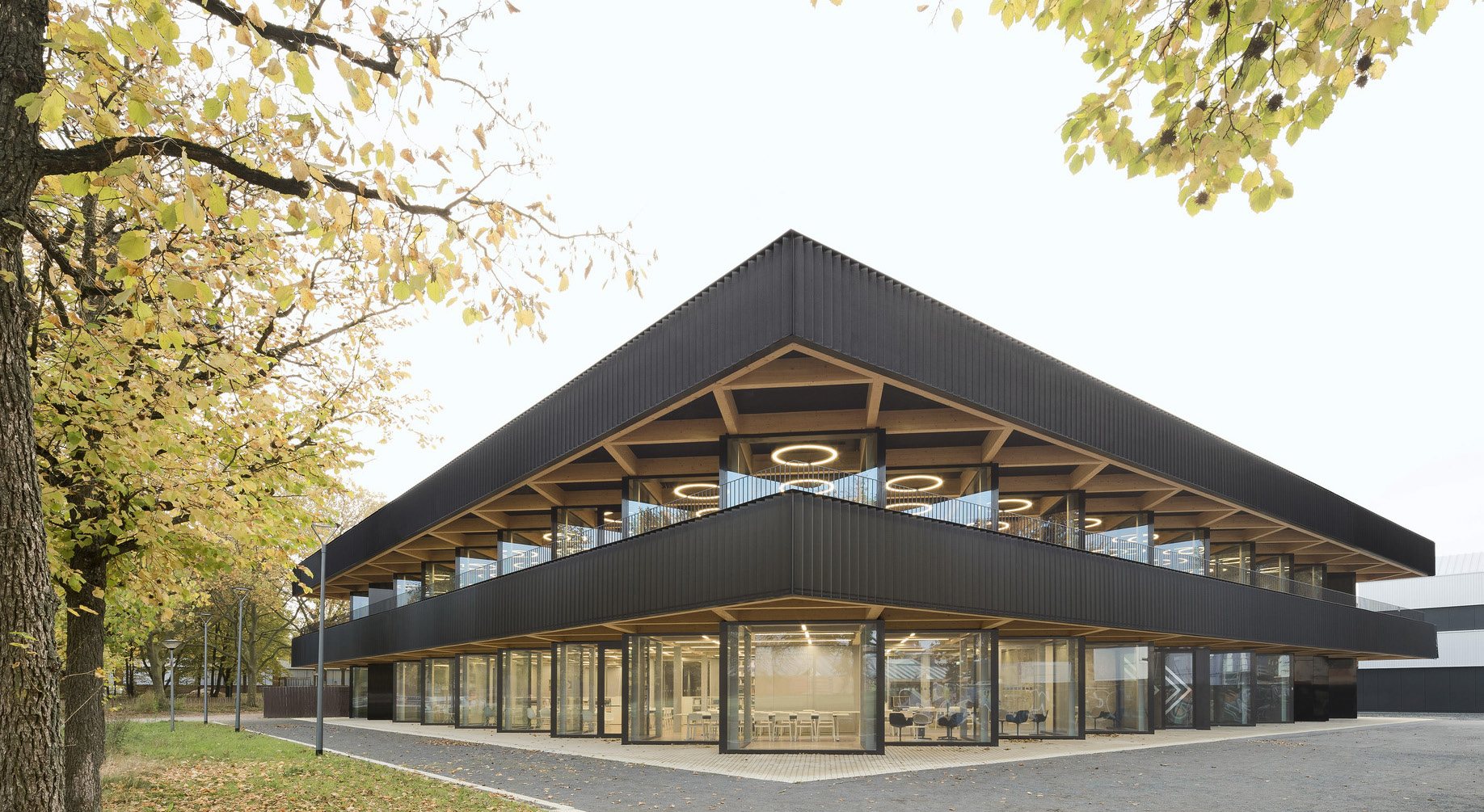 Mensa Berufsschulzentrum Nord - exterior corner view of the black timber-clad building at golden hour